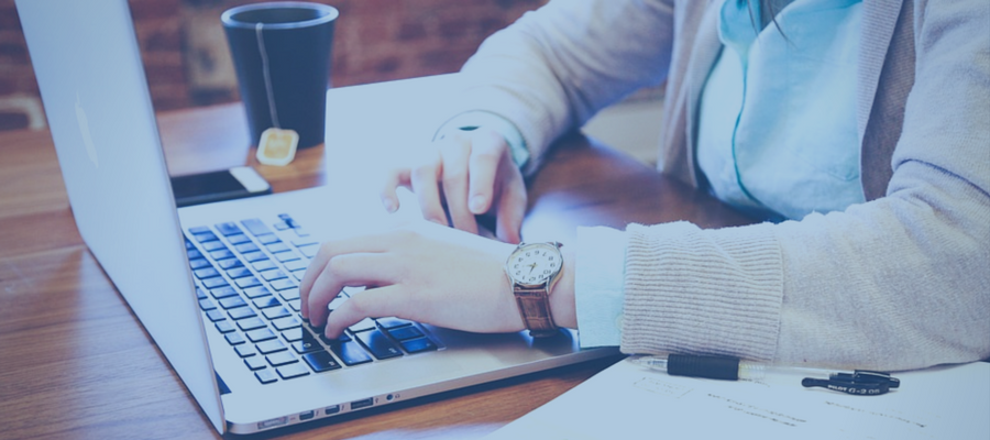 Person typing at computer with coffee